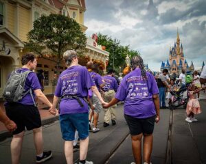 people holding hands walking into disney with castle in background