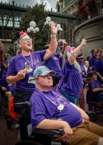 people smiling at disney world parade; staff and man in wheelchair